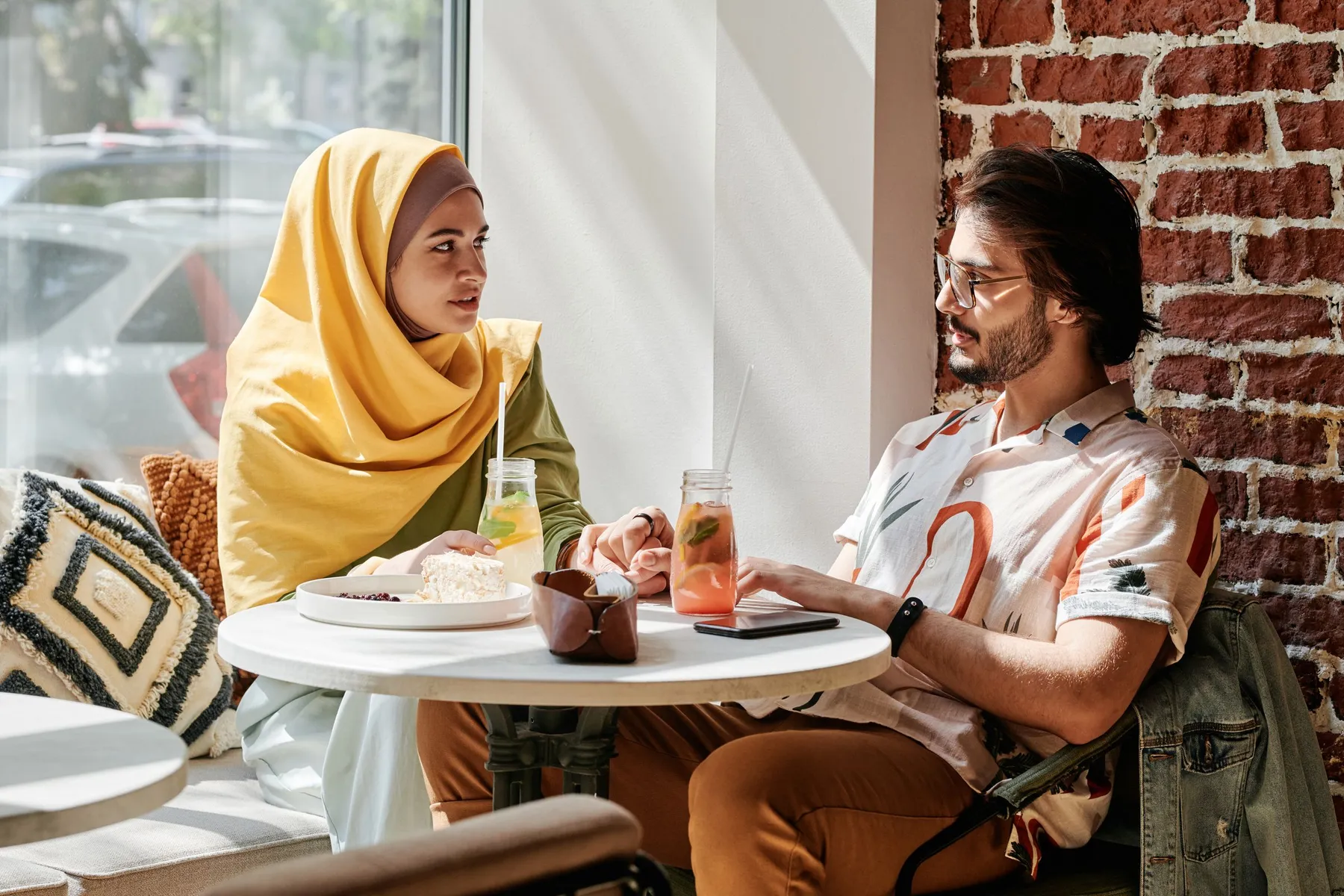 A woman in a mustard hijab and a man chatting over drinks at a café table