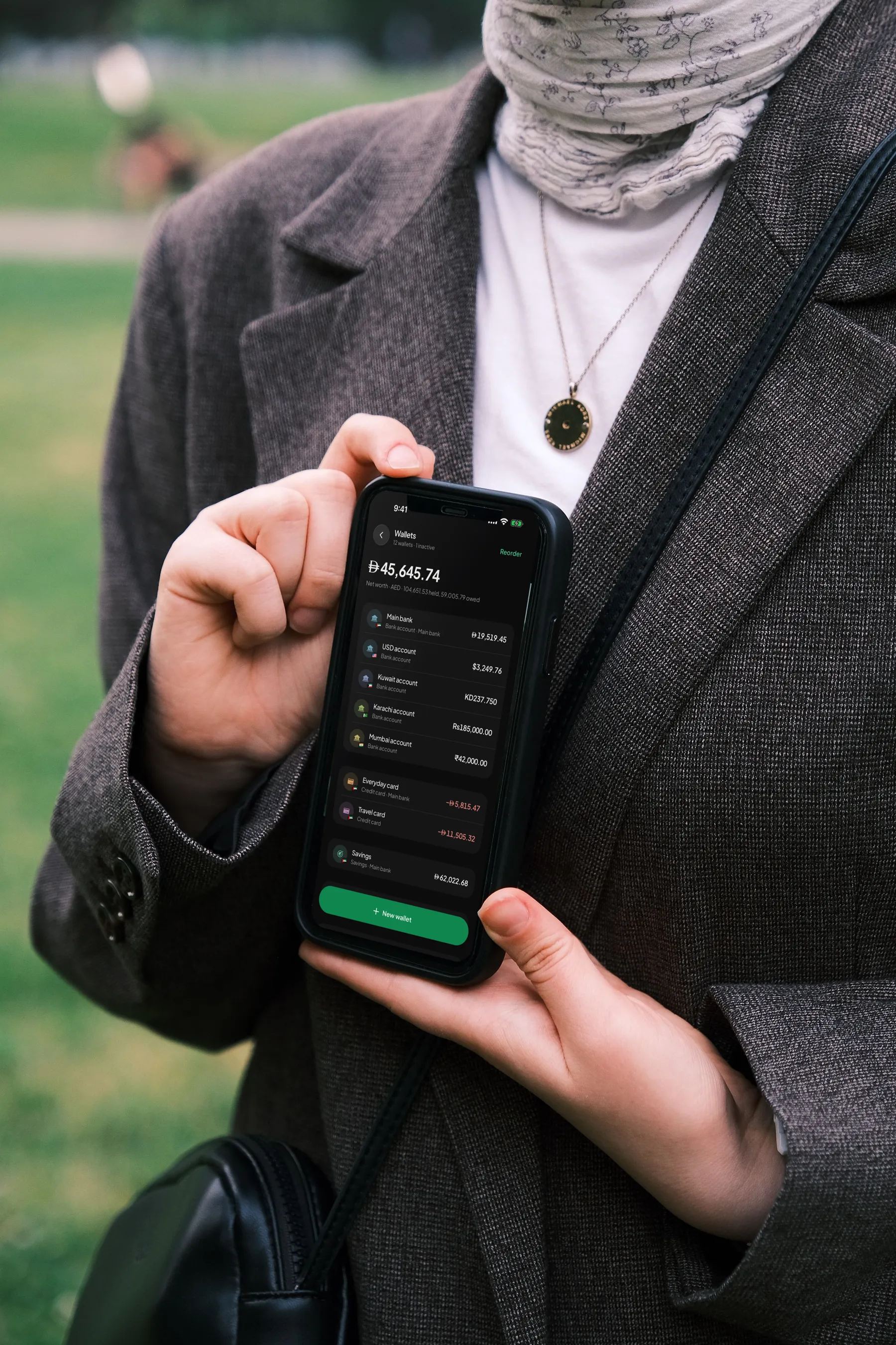 A woman in a hijab holding an iPhone showing Wealthit’s Wallets: accounts in dirhams, dollars, dinars and rupees